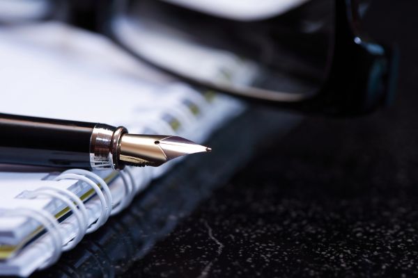 Closeup image of a pen and a pair of glasses sitting on a notebook