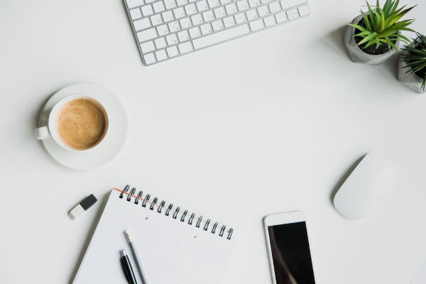 image of white desk with coffee, notepad, pens, and phone